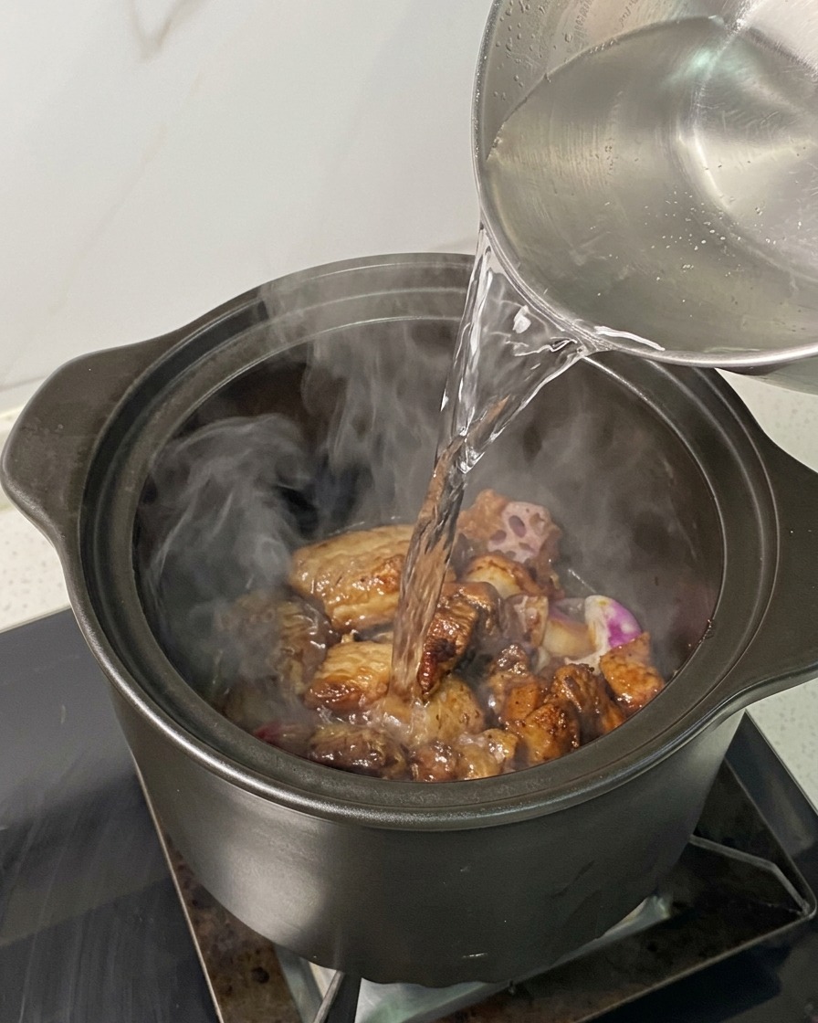 Eau bouillante versée dune bouilloire sur le porc et les échalotes dans la cocotte.