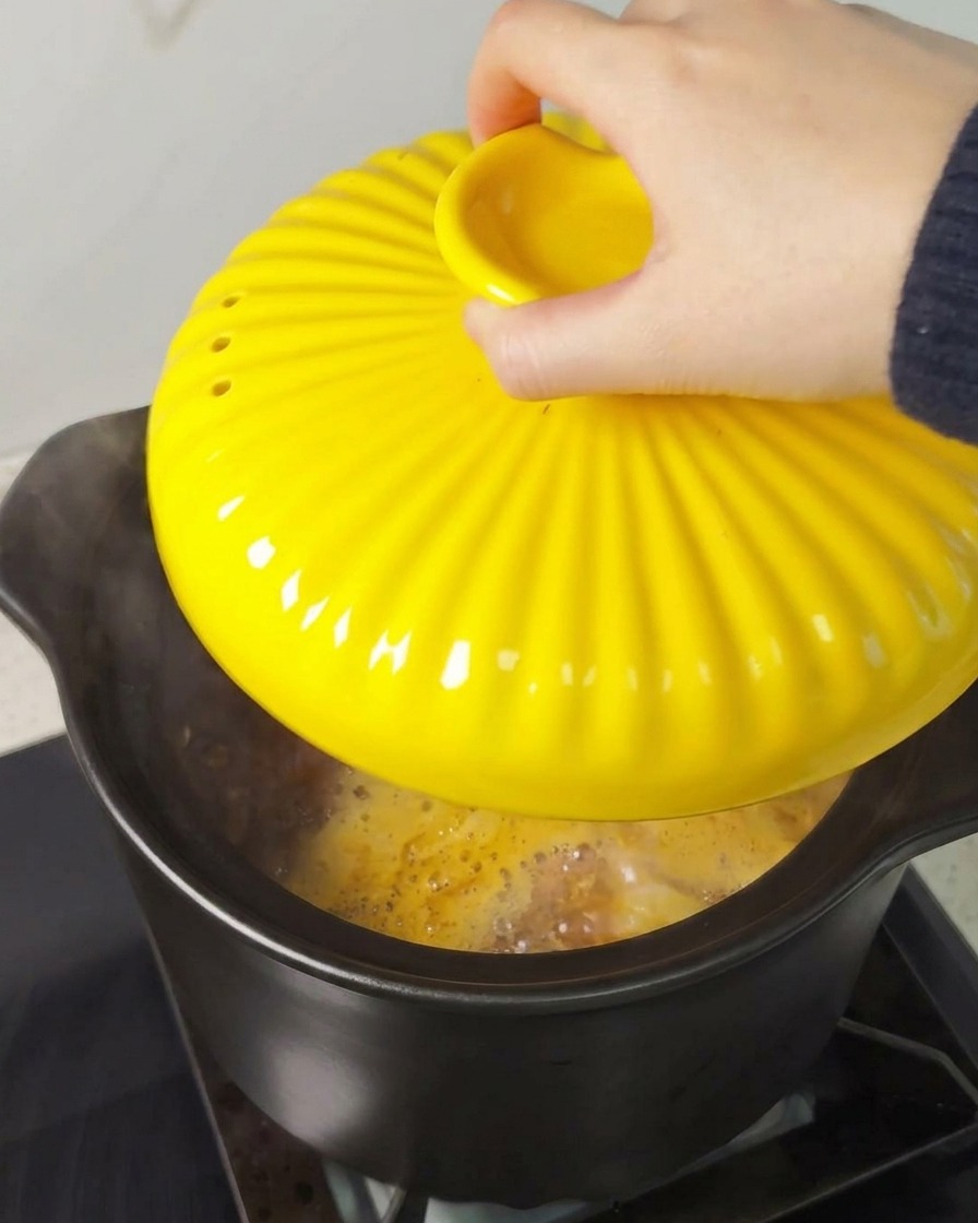 Une main posant un couvercle jaune cannelé sur une cocotte noire sur une cuisinière.