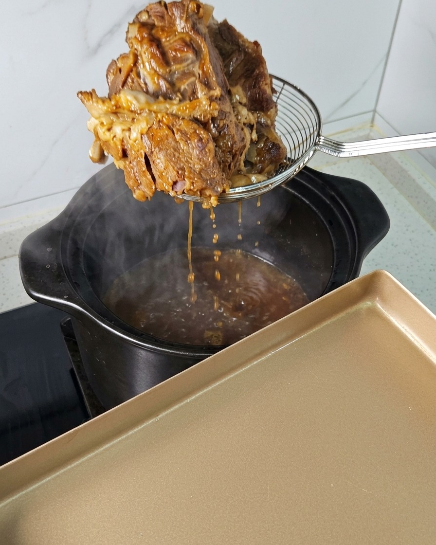 Un gros morceau de porc tendre retiré dune cocotte fumante avec une écumoire.