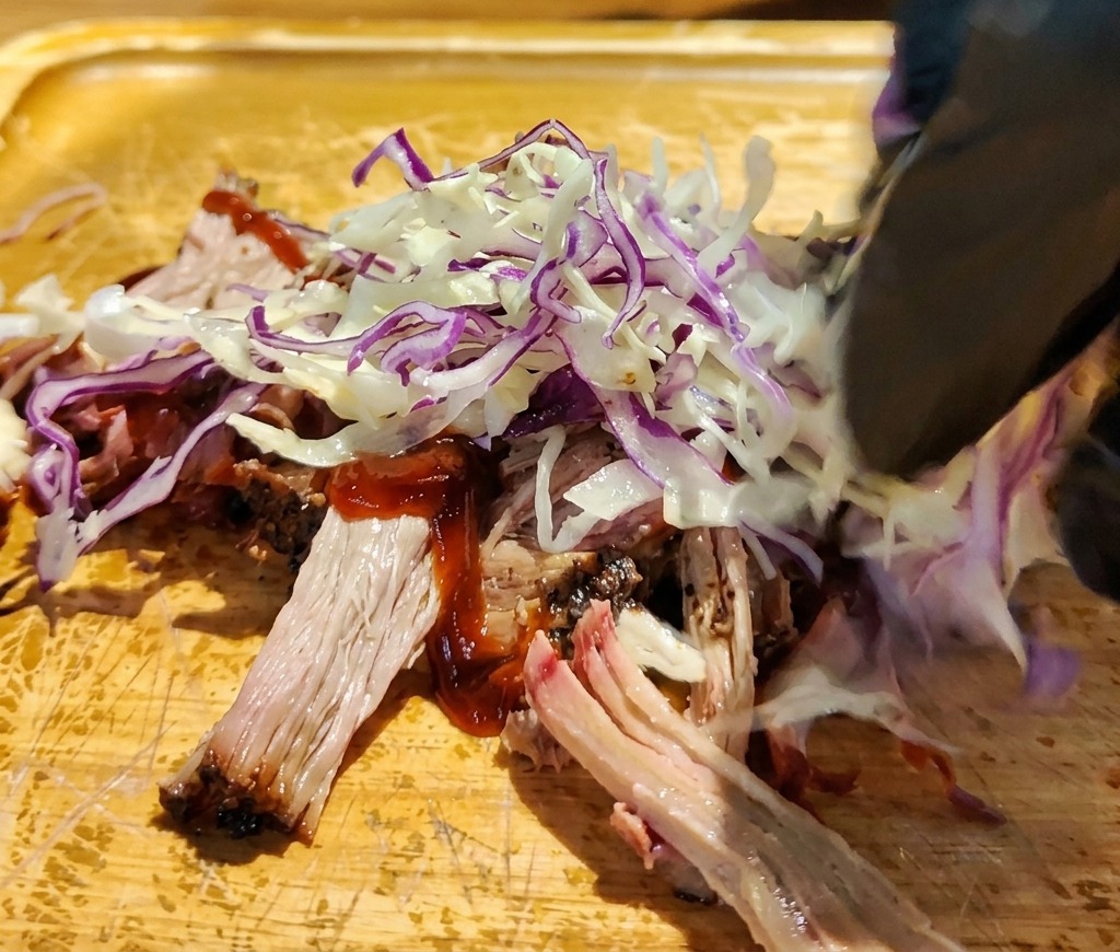 Main déposant du chou rouge et blanc émincé sur le porc effiloché en sauce.
