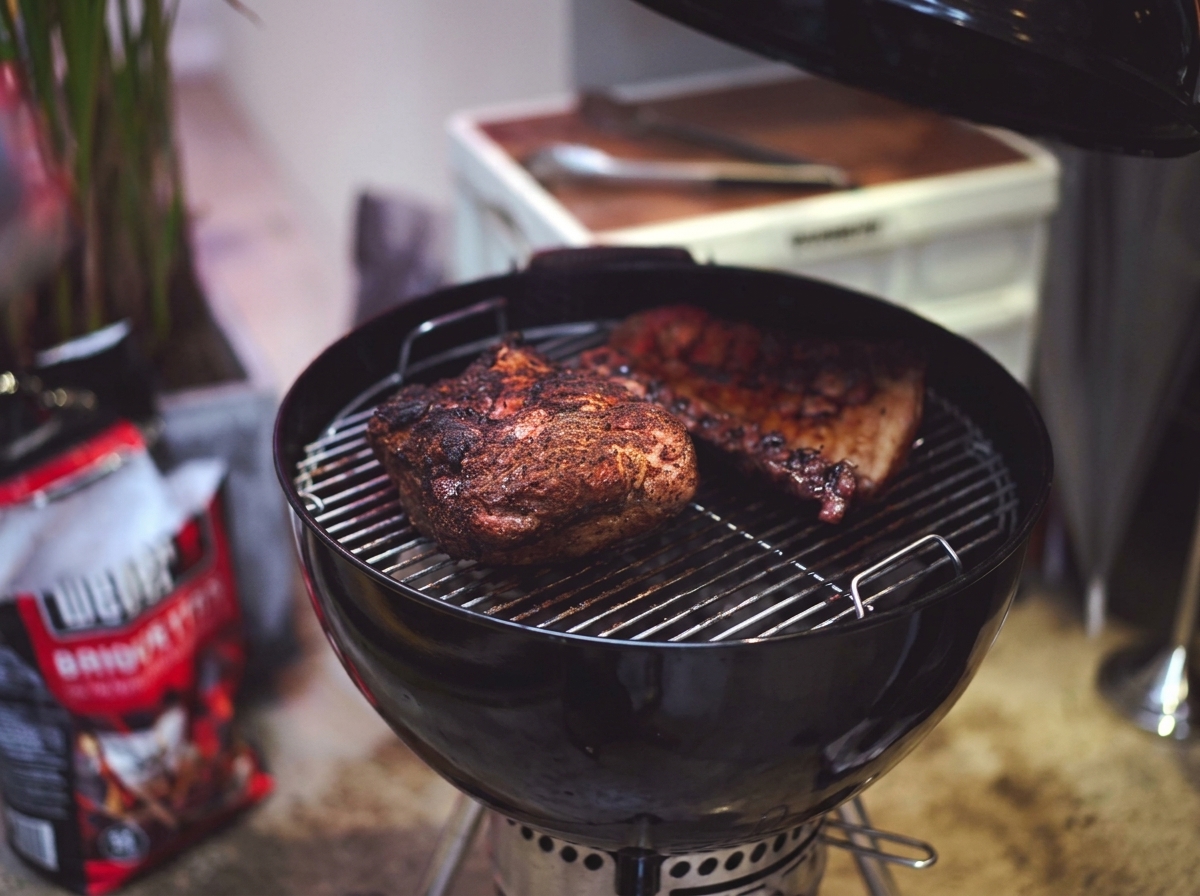 Épaule de porc et ribs partiellement cuits avec une croûte sombre et caramélisée sur la grille du grill.