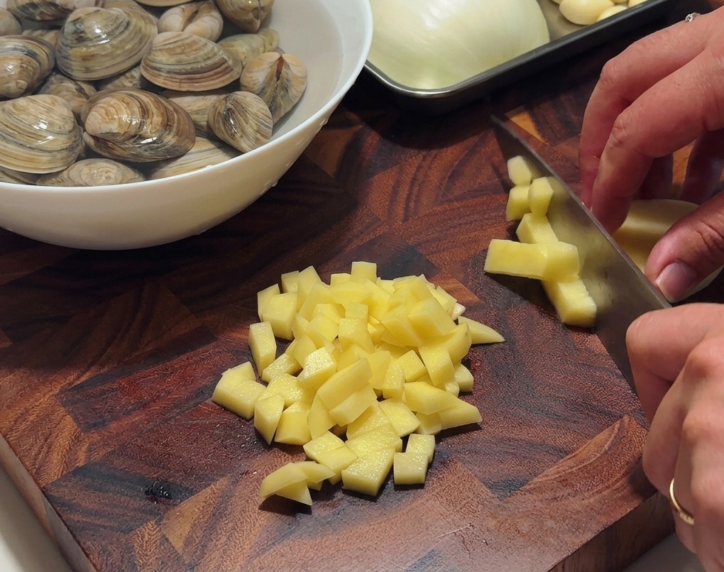 Mains coupant des pommes de terre pelées en petits cubes réguliers sur une planche en bois.