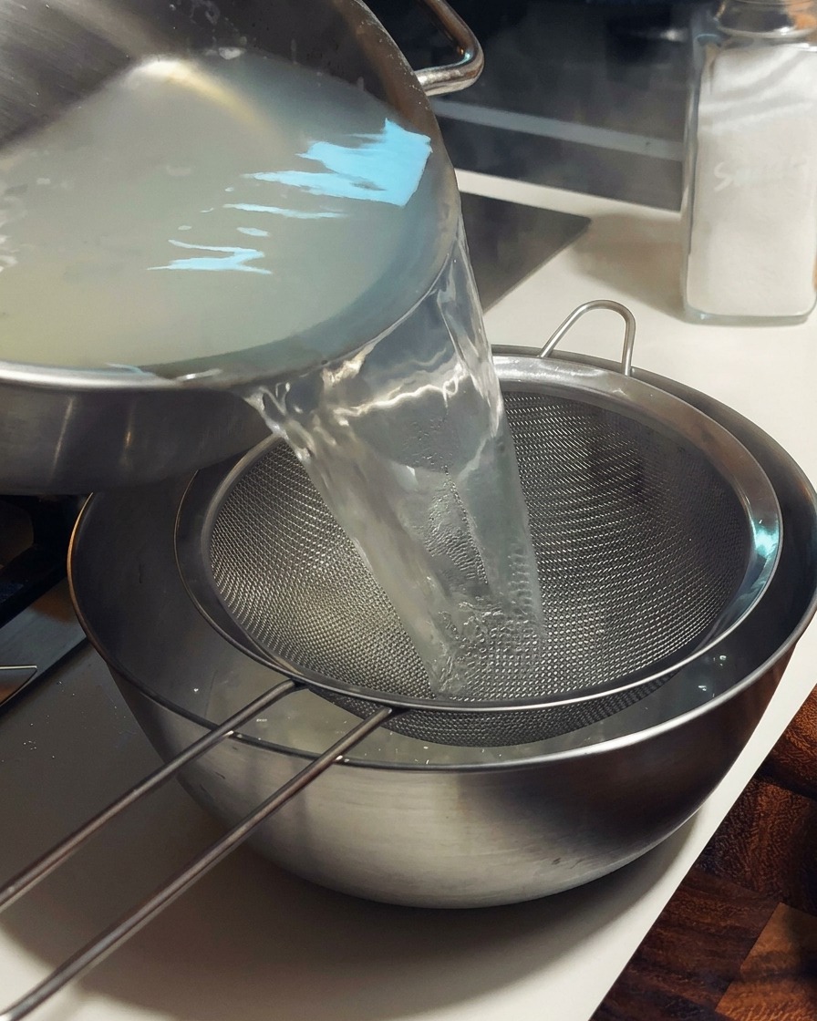 Bouillon de palourde chaud versé à travers une passoire fine dans un bol en métal.