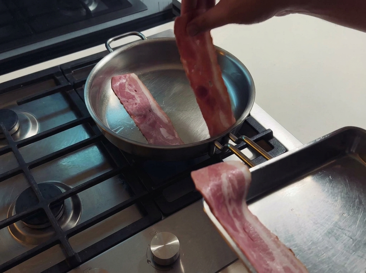 Tranches de bacon grillant dans une poêle en inox et libérant leur gras naturel.