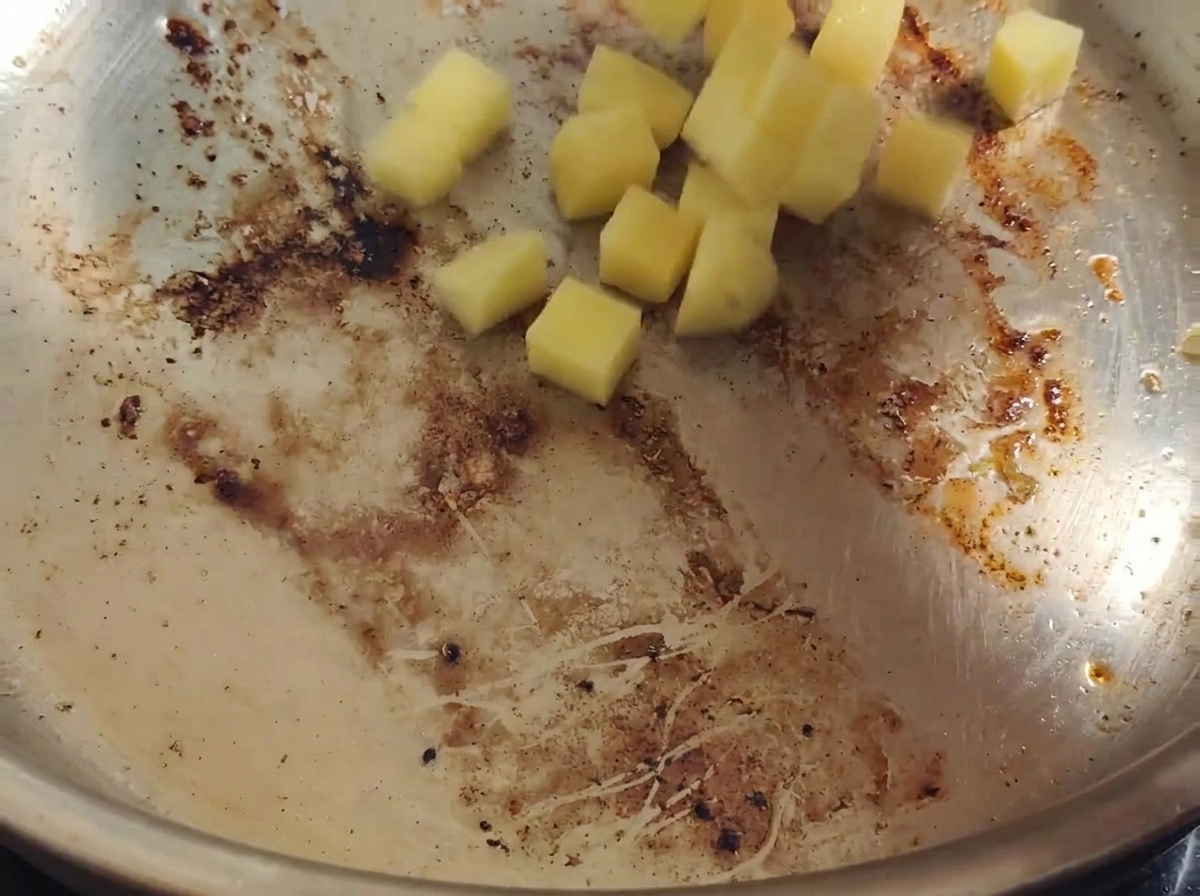 Dés de pommes de terre ajoutés dans une poêle chaude avec du gras de bacon et des sucs de cuisson.