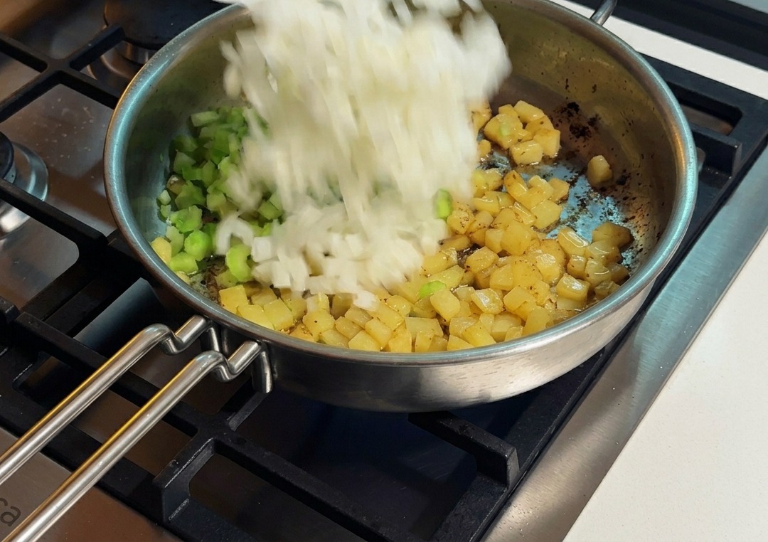 Oignons ajoutés dans la poêle avec le céleri et les pommes de terre déjà dorées.