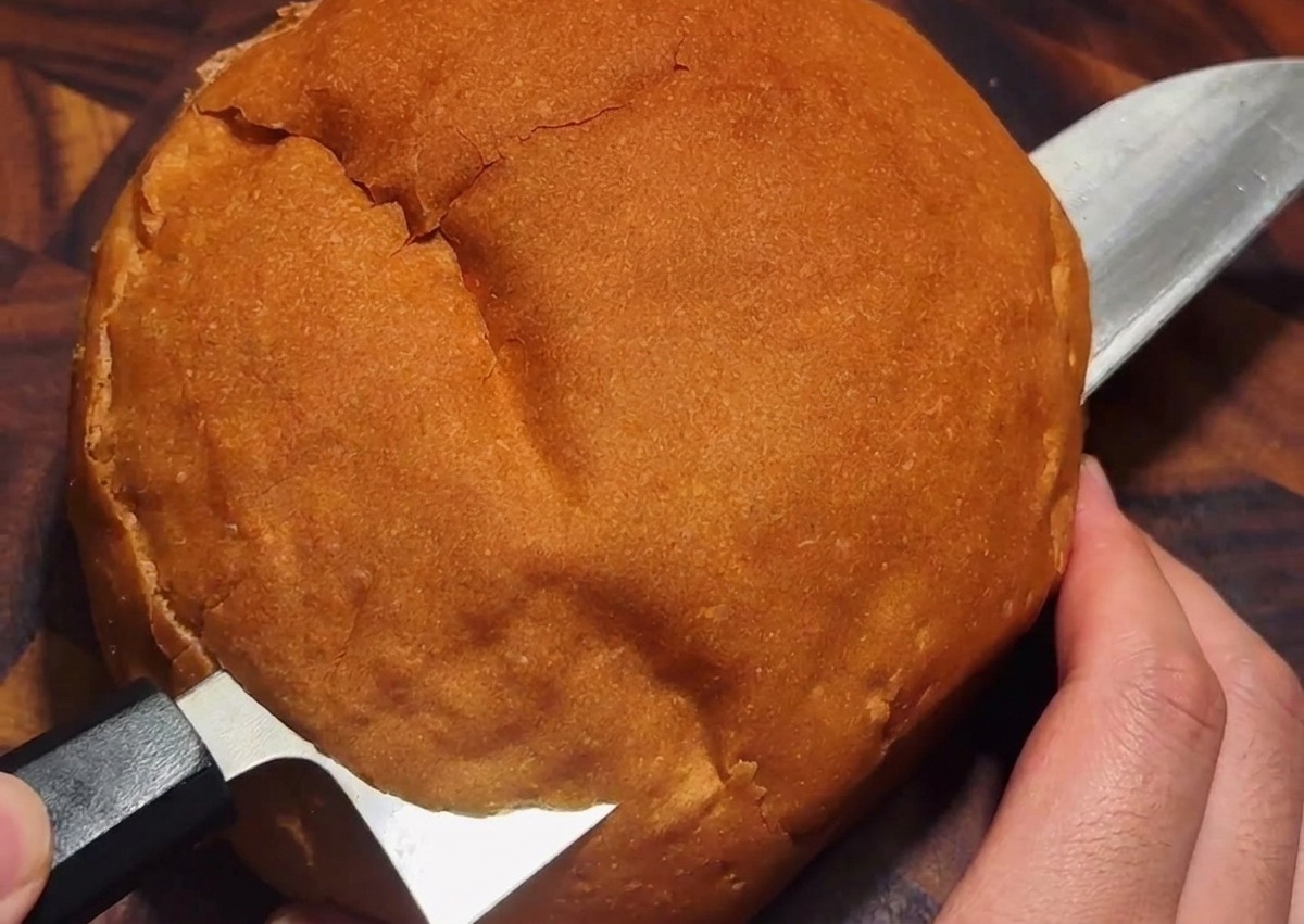 Couteau découpant un chapeau dans une miche de pain ronde sur une planche en bois.