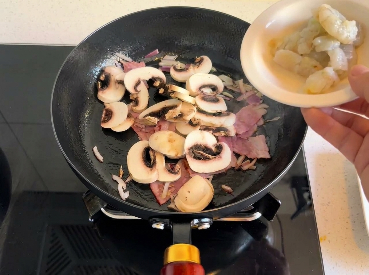 Crevettes crues ajoutées à la poêle avec les lardons et les champignons.