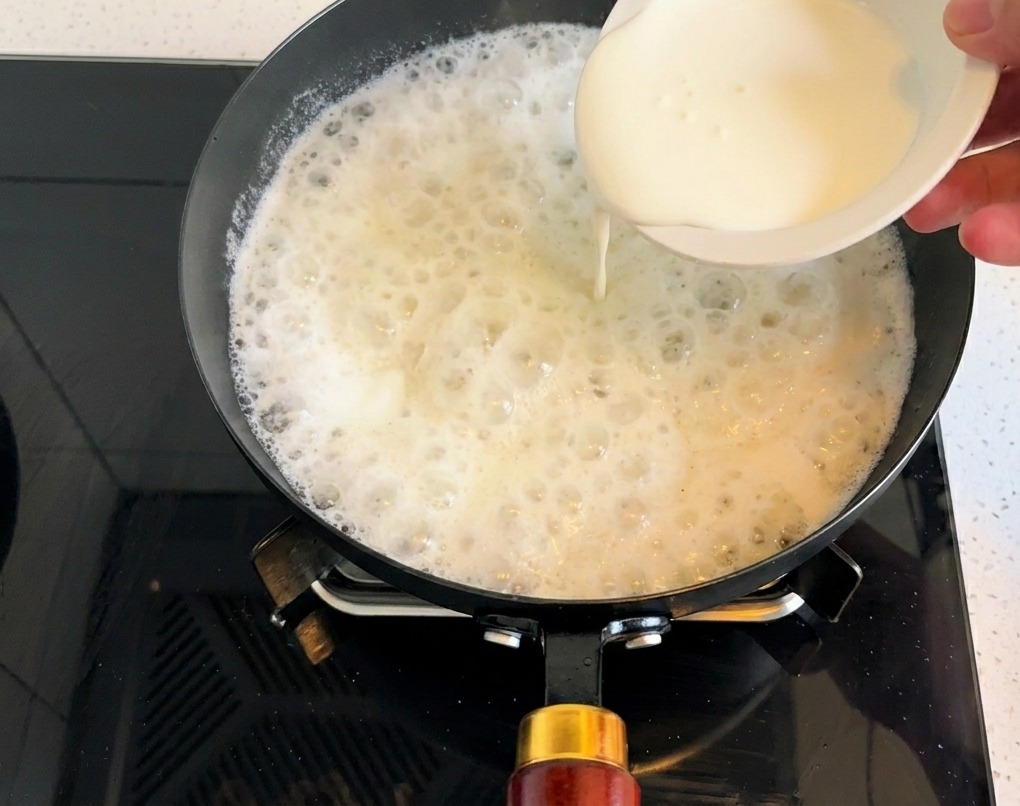 Crème liquide entière versée dans la base de soupe frémissante.