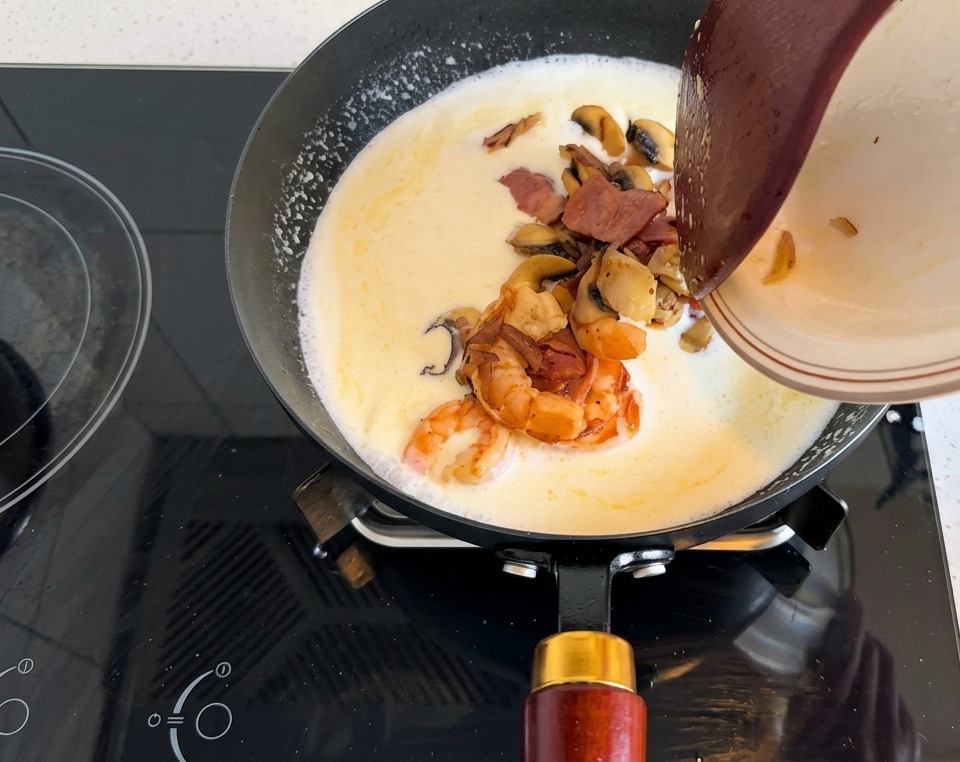 Assiette de crevettes, lardons et champignons versée dans la base crémeuse.