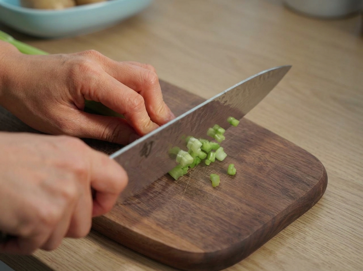 Céleri vert finement coupé en dés sur une planche à découper en bois.