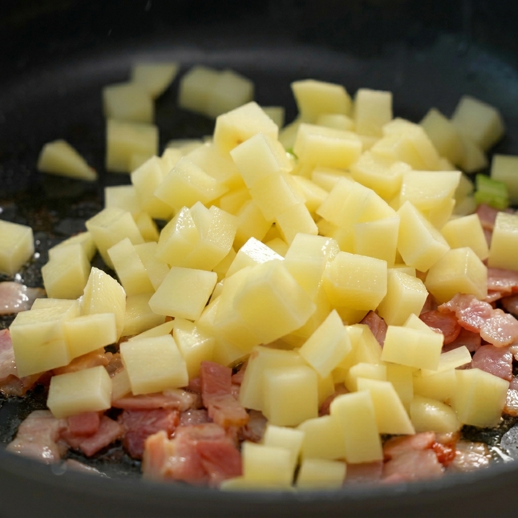 Dés de pommes de terre ajoutés à la poêle contenant le bacon.