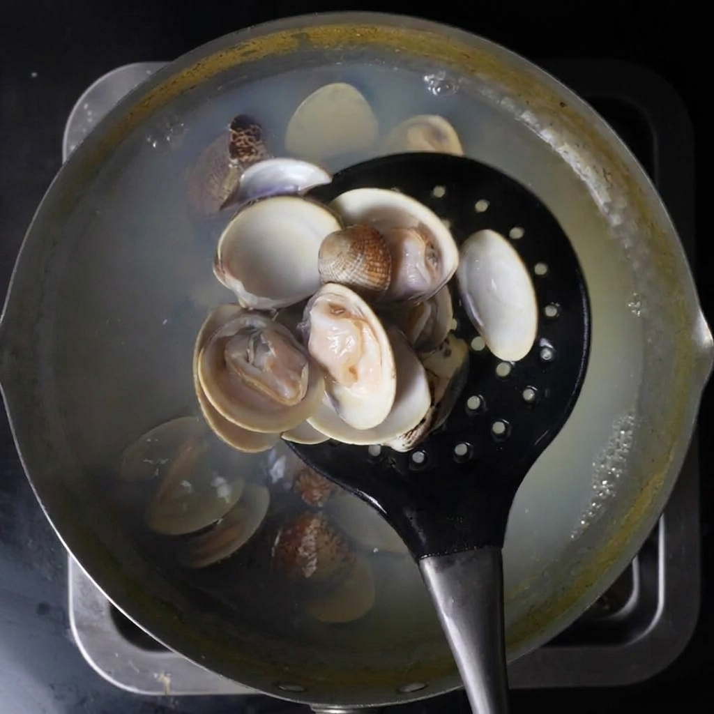 Une écumoire noire sortant des palourdes ouvertes dune casserole deau bouillante.