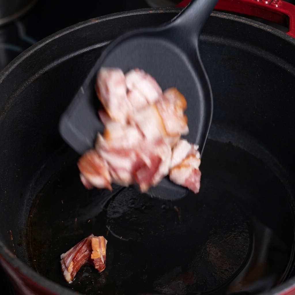 Des morceaux de bacon cru tombant dune spatule noire dans une marmite en fonte chaude.