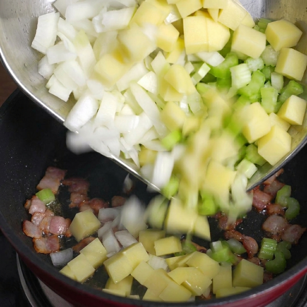 Dés de pommes de terre, de céleri et doignons versés dun bol en métal dans une poêle contenant des morceaux de bacon cuits.
