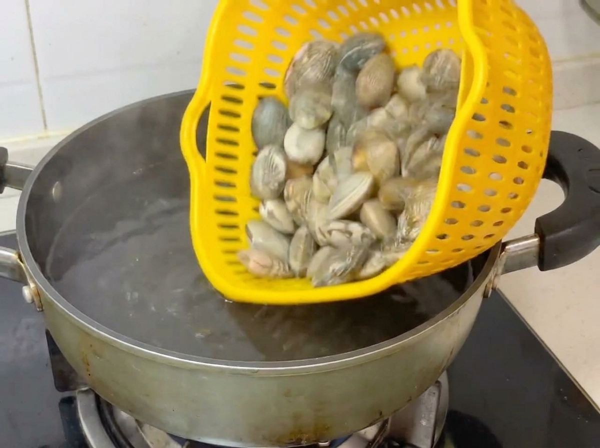 Palourdes entières versées dune passoire jaune dans une casserole deau bouillante.