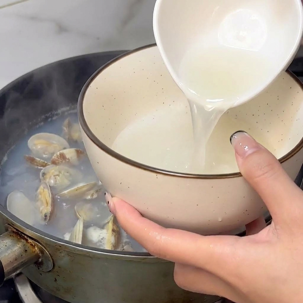 Une main utilisant un bol blanc pour prélever le bouillon de cuisson fumant des palourdes.
