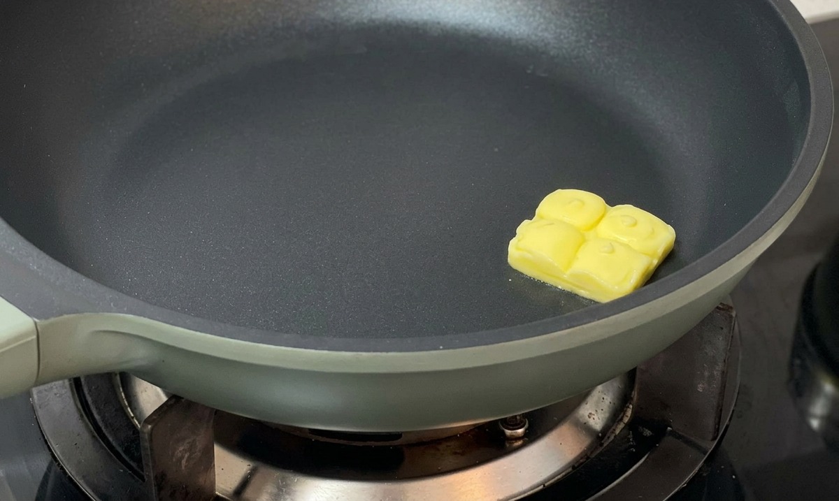 Un morceau de beurre fondant au centre dune poêle antiadhésive foncée.