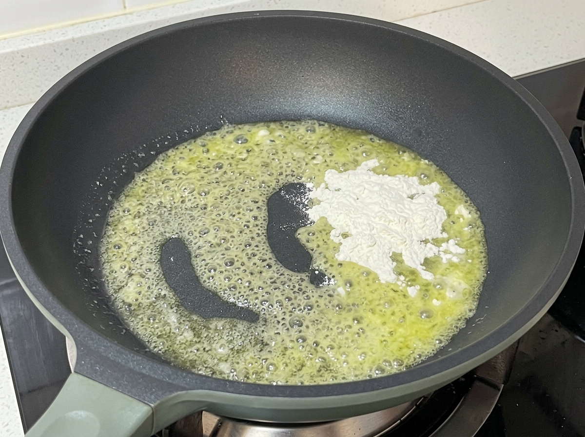 Poêle contenant du beurre fondu moussant avec une pluie de farine blanche en cours de mélange.
