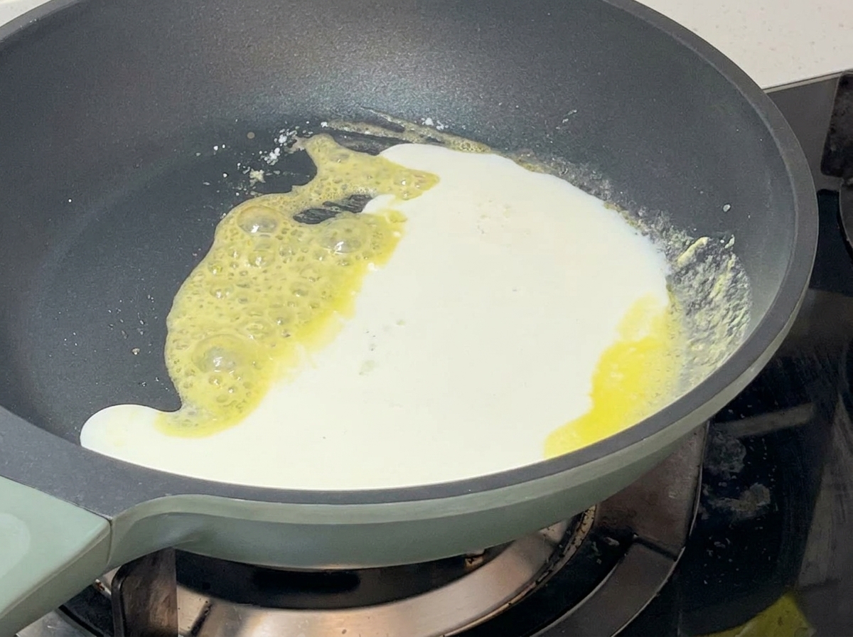 Mélange de lait et crème versé dans la poêle contenant le roux moussant, créant une sauce épaisse.