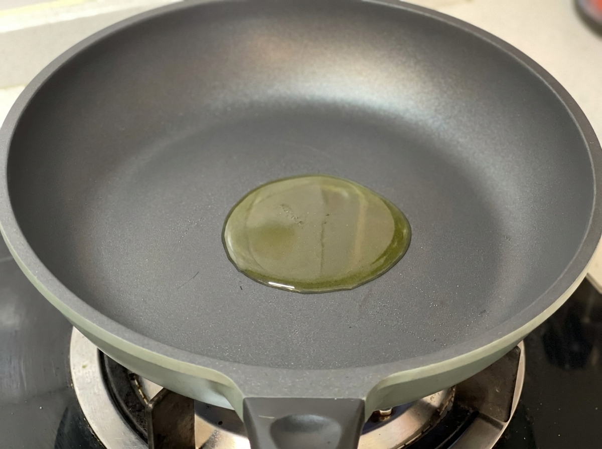 Filet dhuile dolive dorée au centre dune poêle gris foncé sur une cuisinière à gaz.