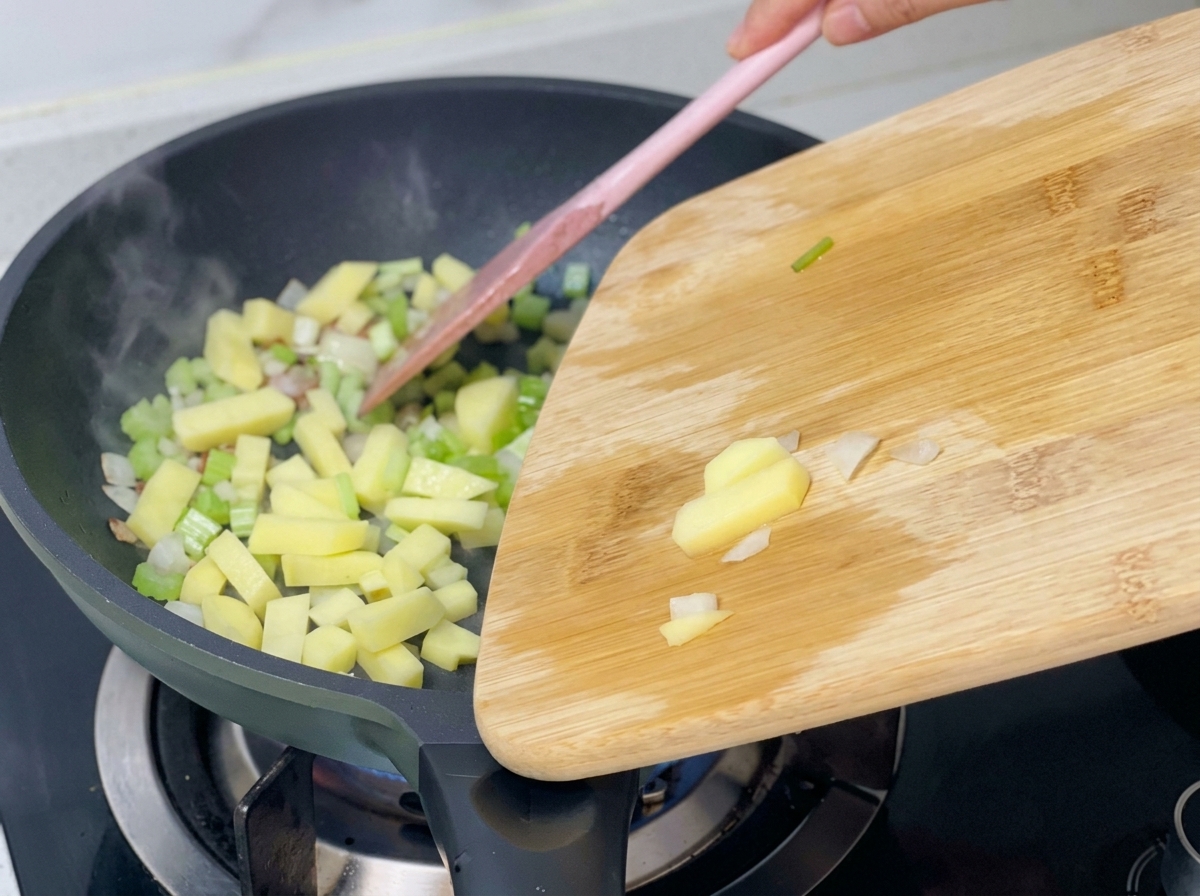 Dés de pommes de terre ajoutés dans une poêle contenant déjà le céleri, les oignons et le bacon sautés.