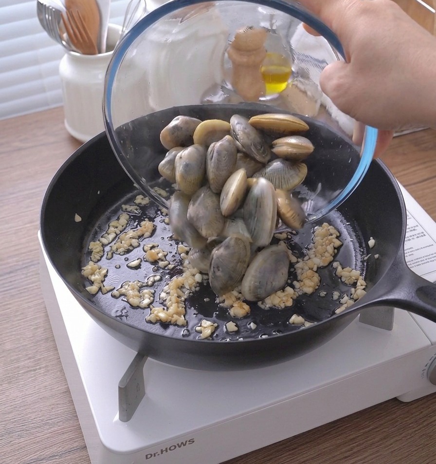Verser les palourdes dun bol en verre dans la poêle contenant lail et le beurre.