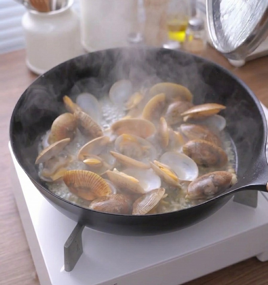 Vapeur séchappant dune poêle de palourdes cuites avec leurs coquilles ouvertes.
