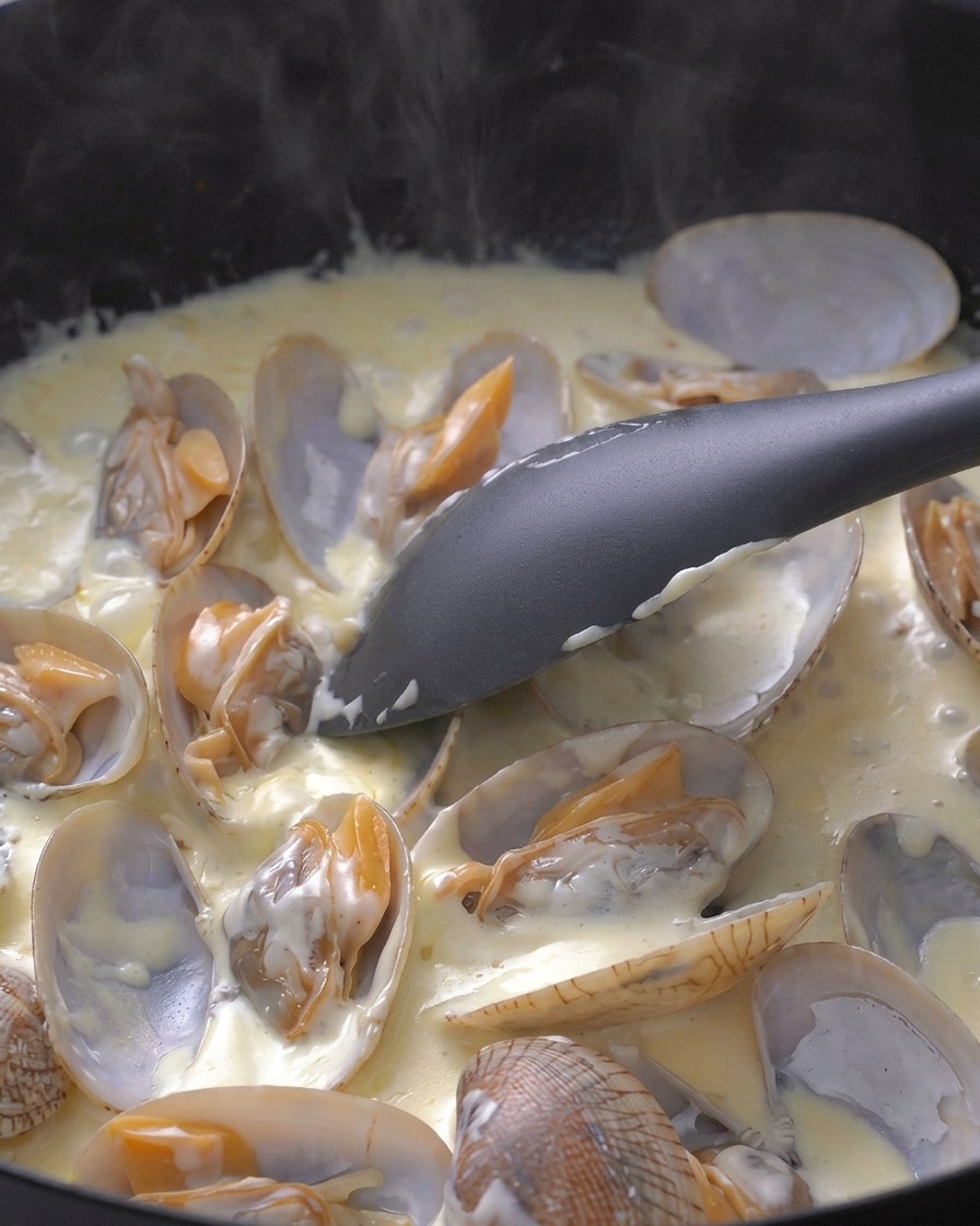 Spatule remuant les palourdes dans une sauce blanche bouillonnante.