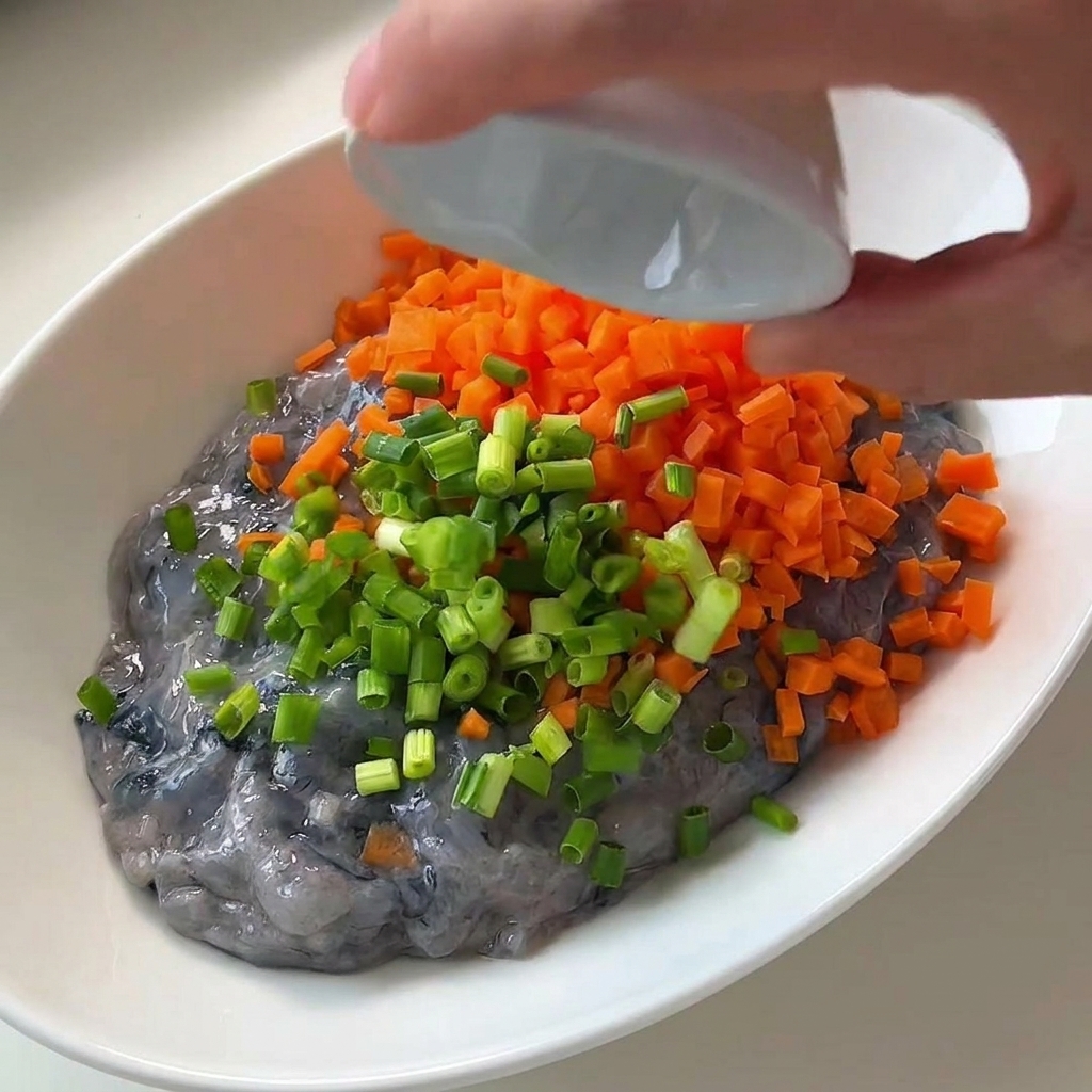Oignons verts hachés versés sur la pâte de crevettes et les carottes dans un bol.