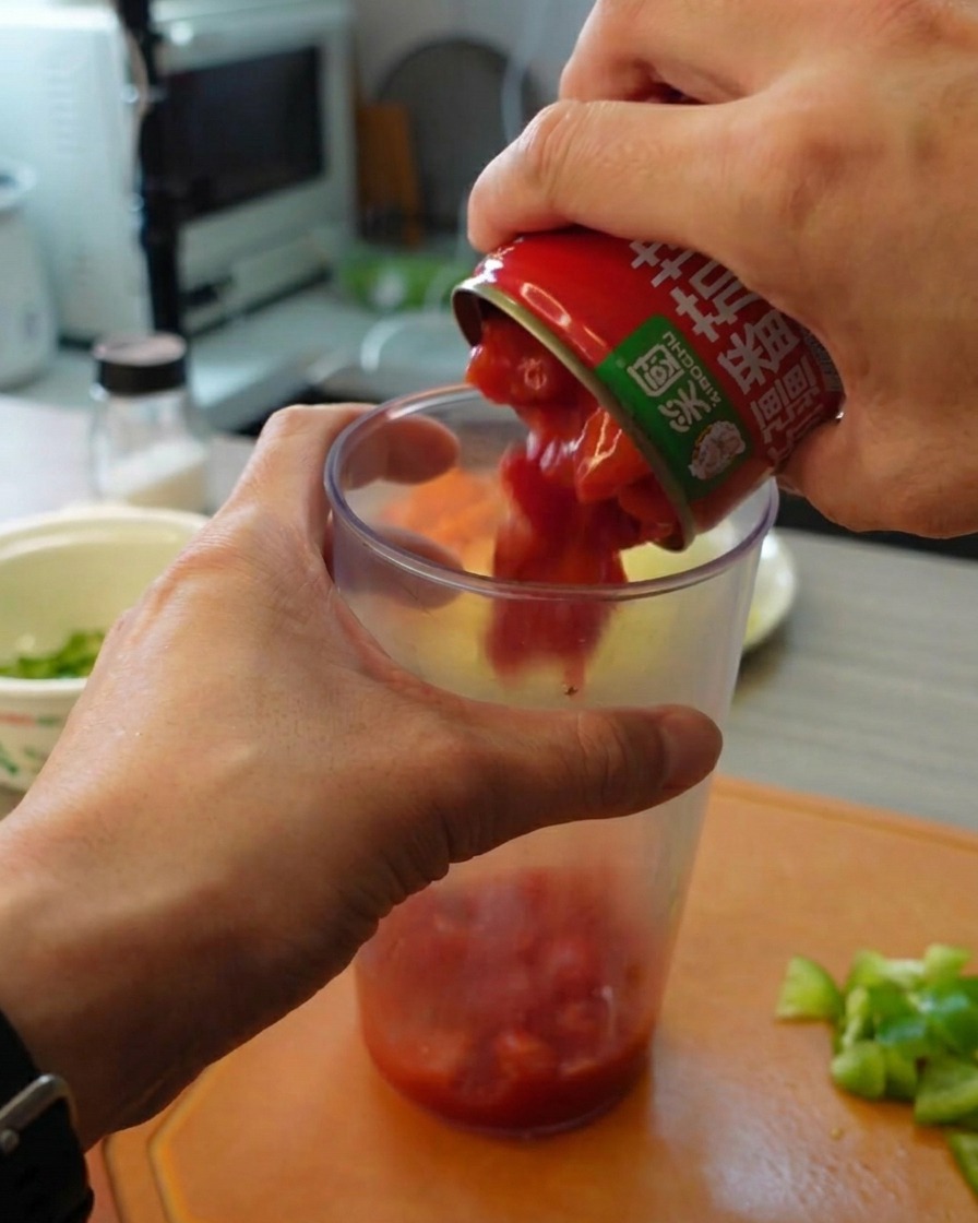Mains versant une boîte de tomates concassées dans un grand récipient mixeur en plastique transparent.