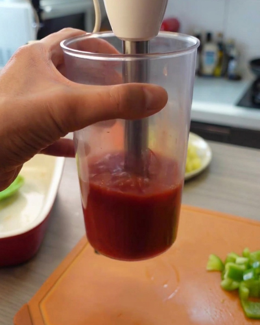 Mixeur plongeant utilisé pour réduire les tomates en conserve en purée dans un récipient en plastique haut.