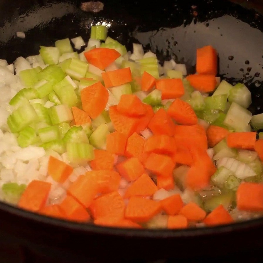 Vue de dessus dune poêle avec oignons, céleri et dés de carottes oranges en cours de cuisson.