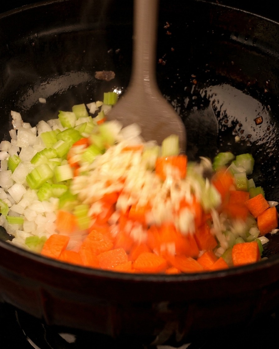 Dés de carottes ajoutés dans une poêle contenant déjà des oignons et du céleri sautés.
