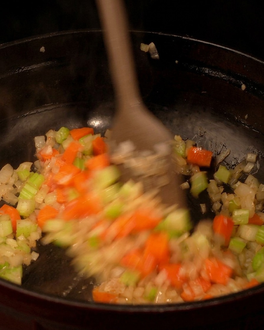 Spatule en bois mélangeant les légumes colorés dans une poêle noire.