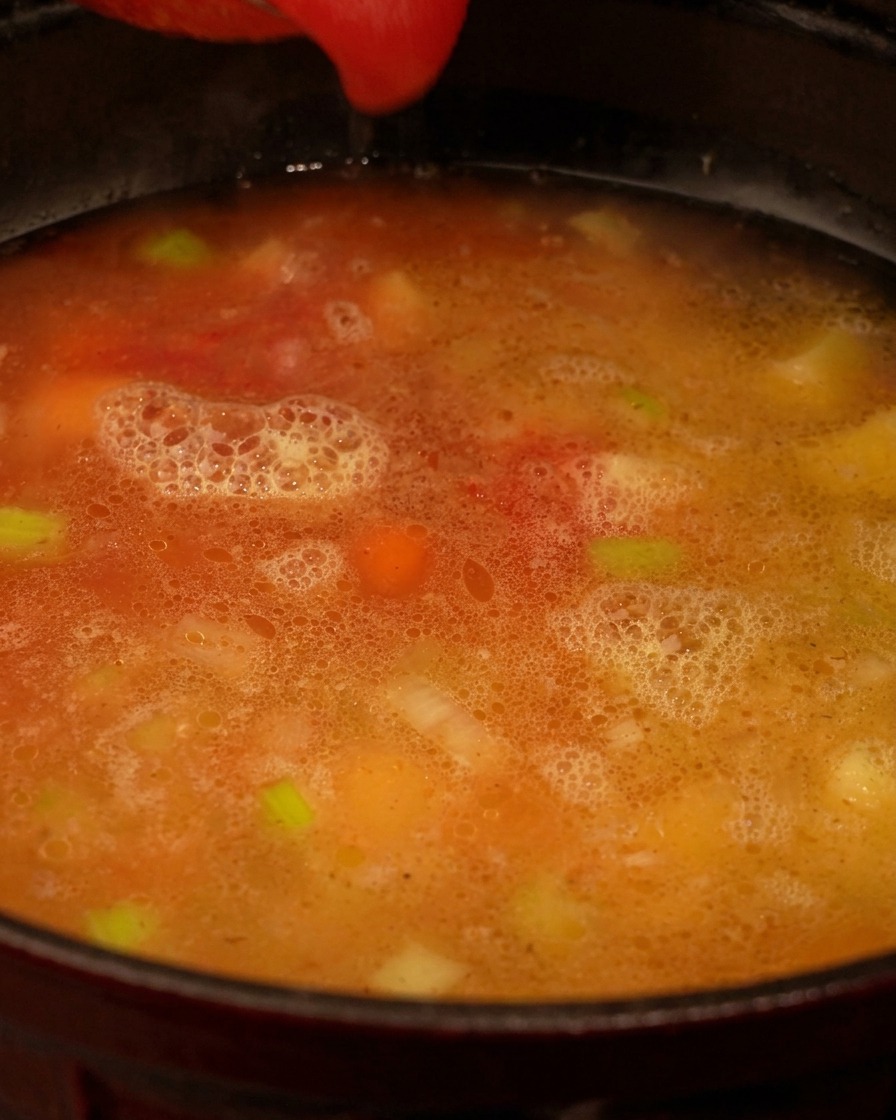 Purée de tomates rouge versée dans une marmite contenant le bouillon et les légumes.