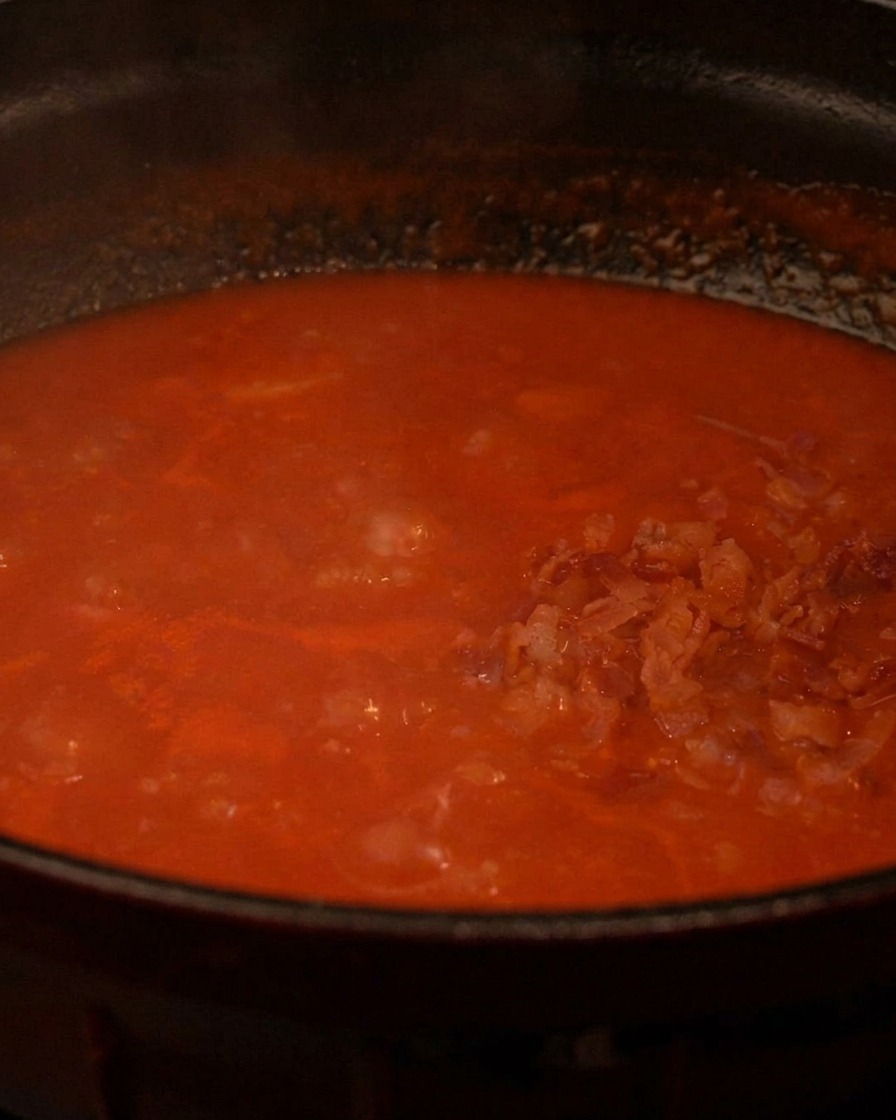 Morceaux de bacon croustillants ajoutés à la soupe de tomate bouillonnante.