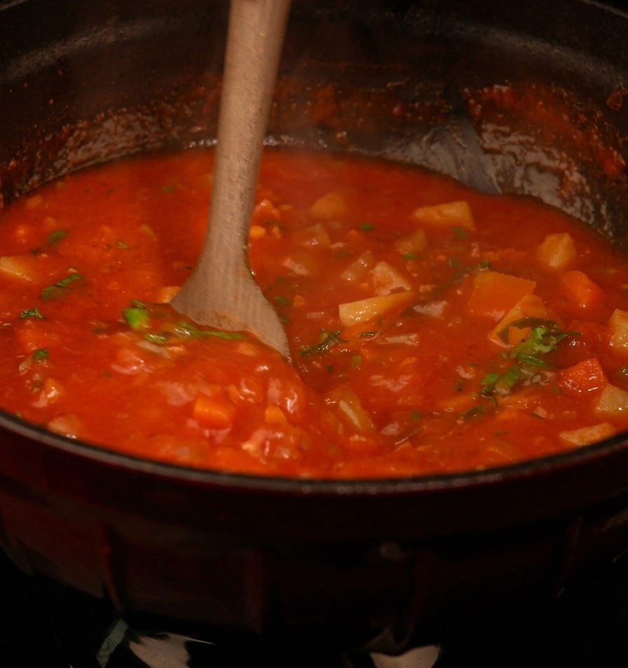 Cuillère en bois mélangeant une soupe épaisse à la tomate parsemée de persil frais.