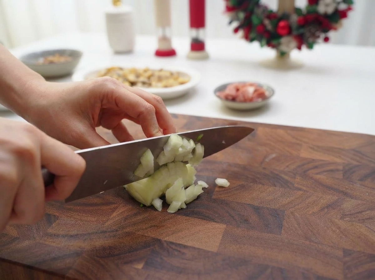 Mains utilisant un couteau de chef pour couper un oignon blanc en petits morceaux sur une planche à découper en bois.