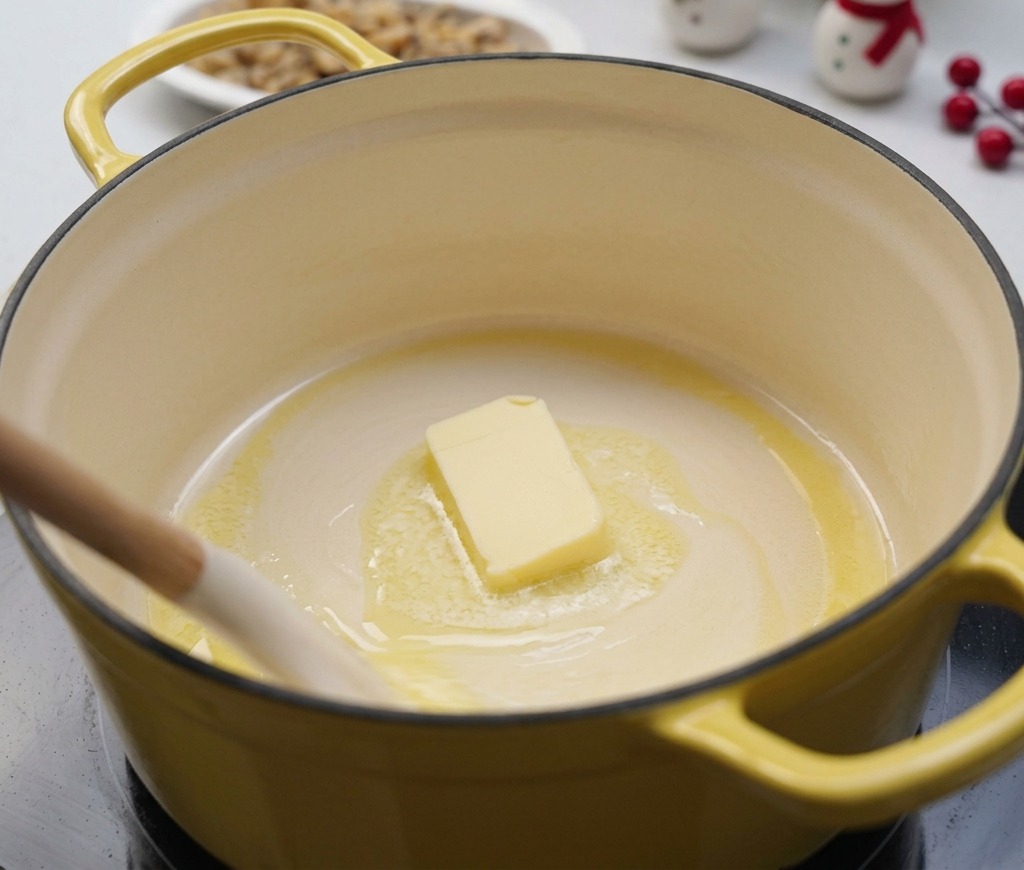 Un bloc de beurre fondant dans une marmite jaune à feu doux, remué doucement par une spatule blanche.