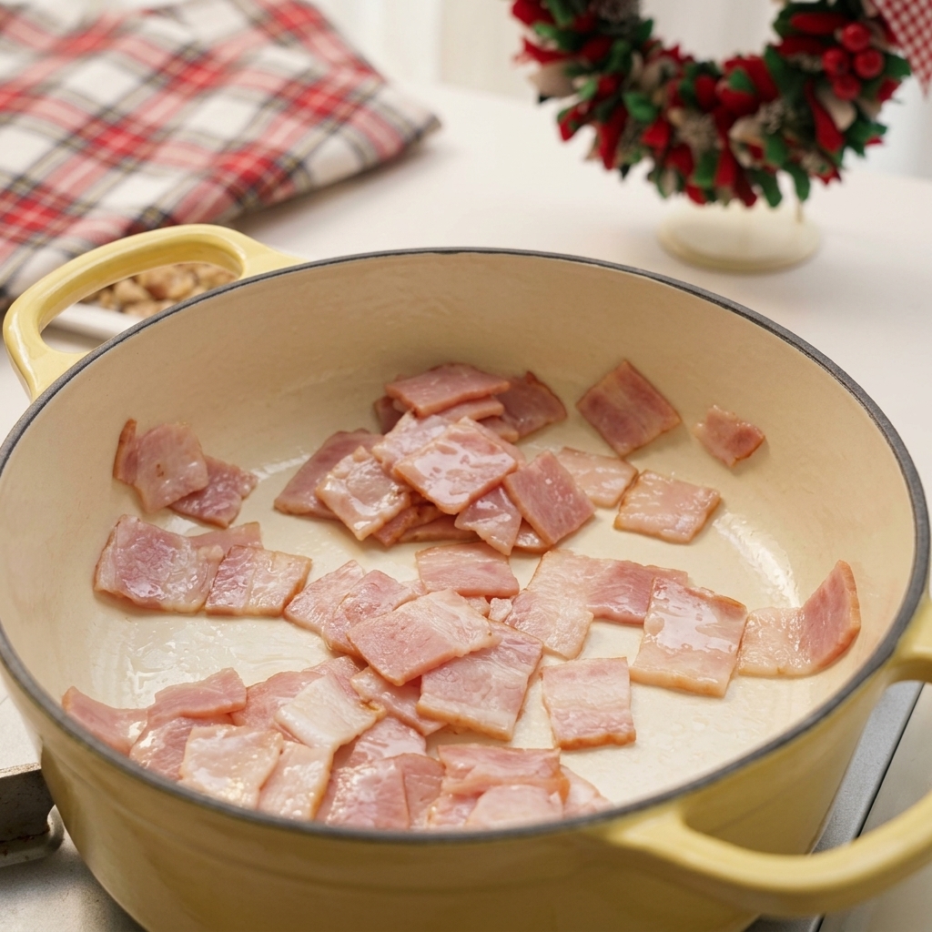 Carrés de bacon hachés en train de frire dans une marmite en émail jaune pâle.