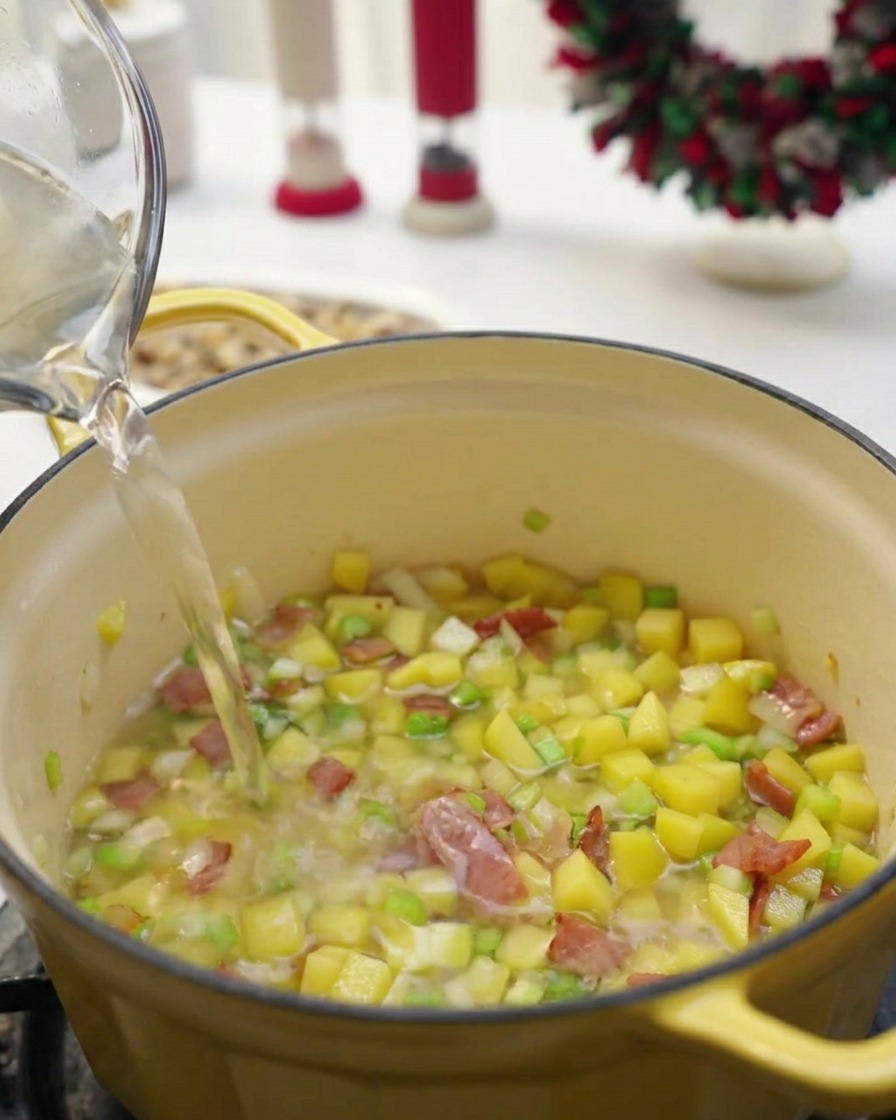 Un liquide clair versé dun pichet en verre dans une marmite jaune contenant des légumes en dés et du bacon.