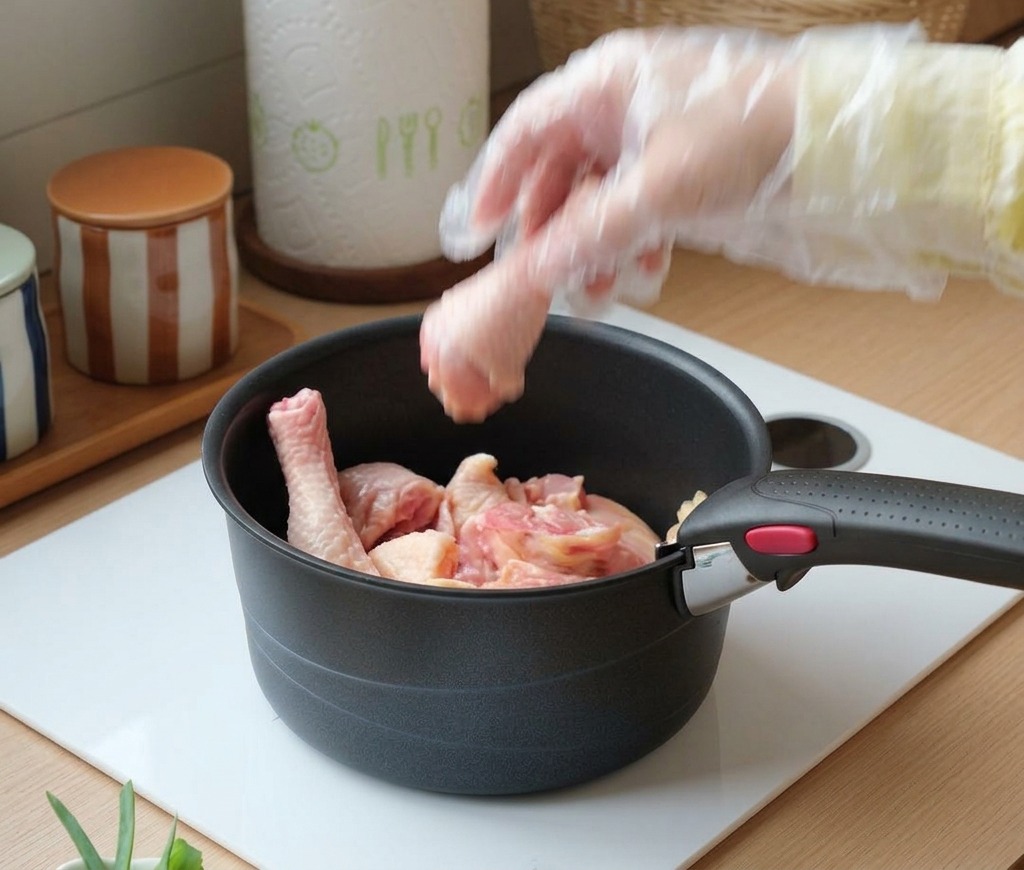 Une main gantée plaçant des pilons de poulet crus dans une marmite noire.