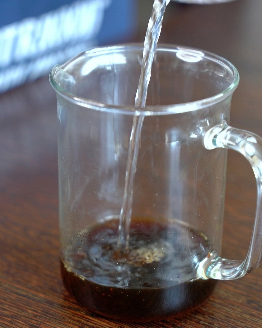 De leau claire versée dans un verre doseur contenant le mélange de sauce soja infusée au kombu et de sucre.