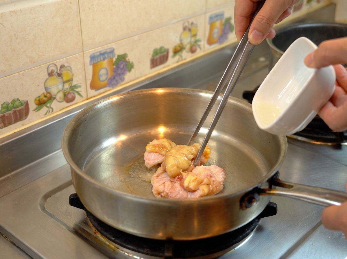 Morceaux de gras de poulet crus manipulés avec une pince dans une poêle en inox pour les faire fondre en huile.
