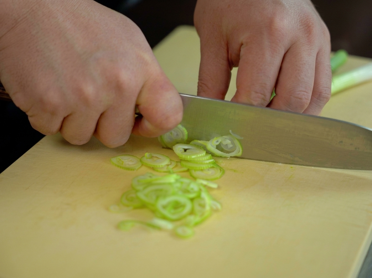 Mains hachant finement des oignons verts frais en fines rondelles avec un couteau de chef.