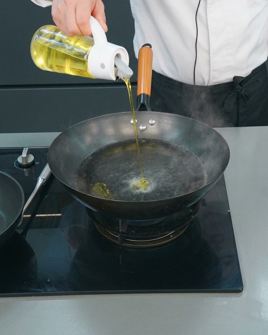 Un chef versant un mince filet dhuile de cuisson dans un wok deau bouillante.