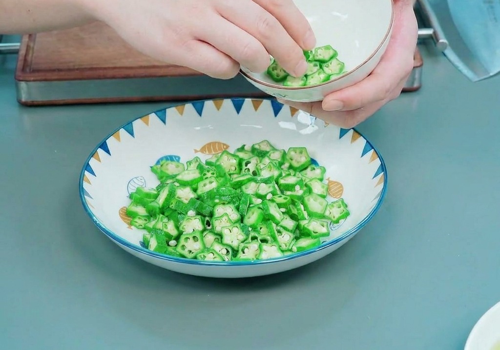 Mains tapissant soigneusement lintérieur dun petit bol blanc avec des tranches de gombo en forme détoile.