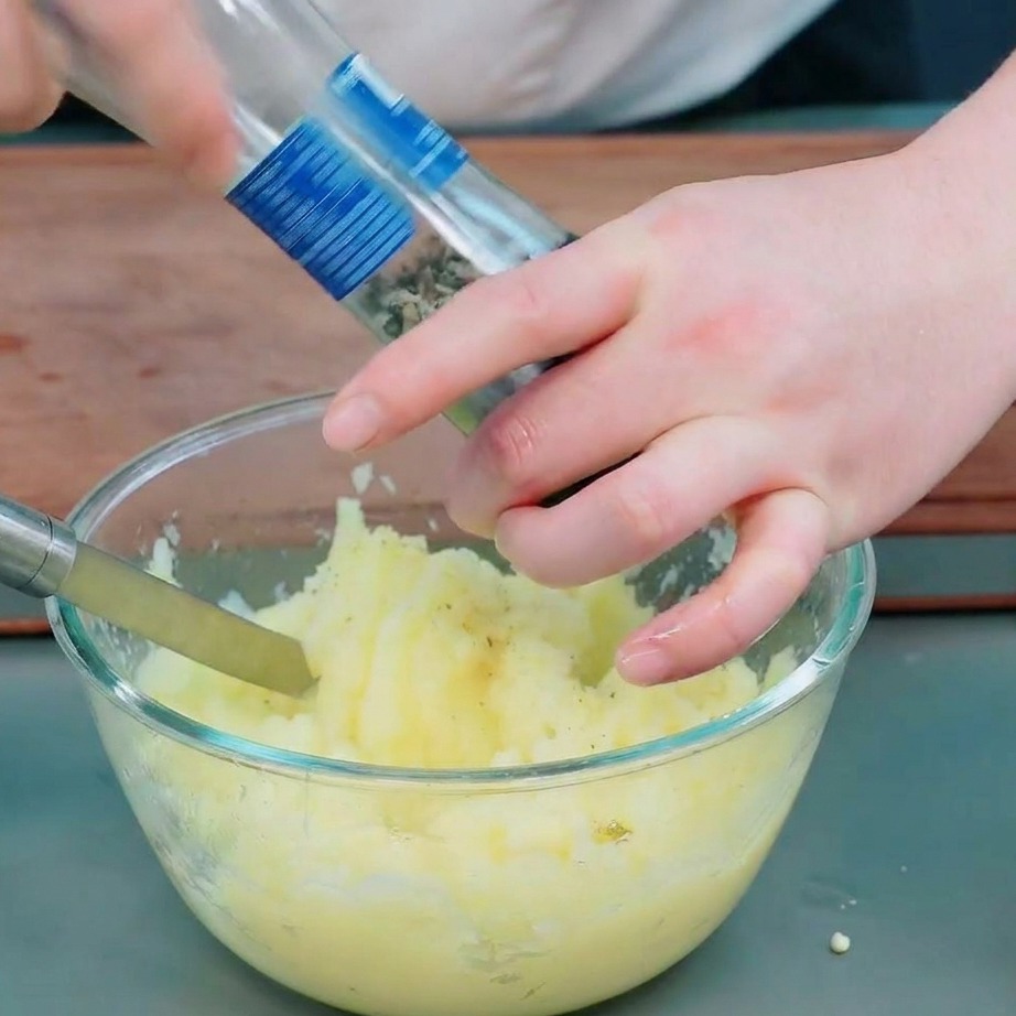 Mains utilisant un moulin pour ajouter du poivre noir et du sel à une purée de pommes de terre lisse.