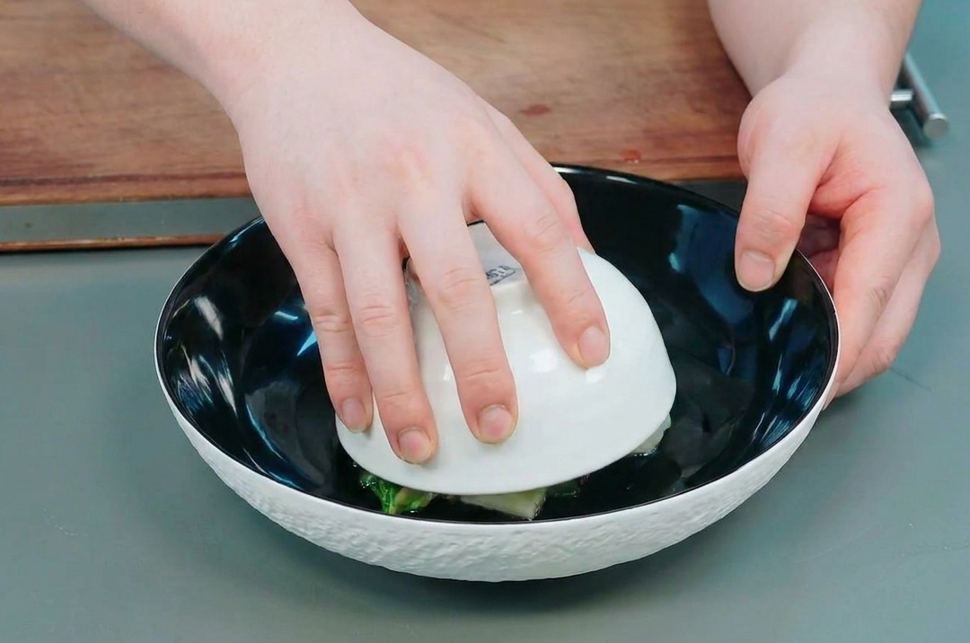 Mains soulevant délicatement un petit bol blanc pour révéler le dôme de gombo et pomme de terre dans un plat de service.